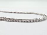 un gros plan d'un bracelet « tennis » en diamants posé sur une surface blanche