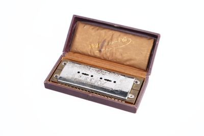 un harmonica argenté dans un étui en bois posé sur une surface blanche