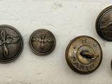 six boutons anciens en laiton posés sur un morceau de papier blanc