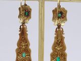 pair of gold and emerald earrings on a gold plated stand