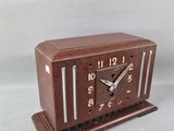 a small wooden clock on a stand on a white surface