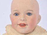 a small doll with blue eyes sitting on a white surface