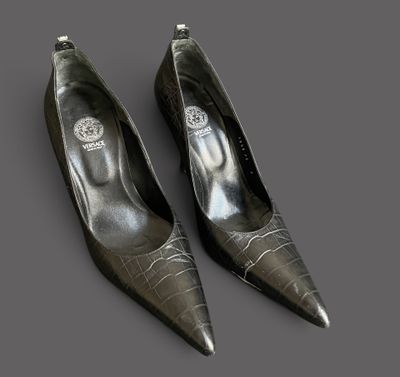 two pairs of black shoes with silver heels on a gray surface