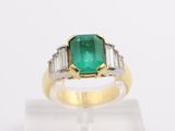 an emerald and diamond ring on display on a clear surface
