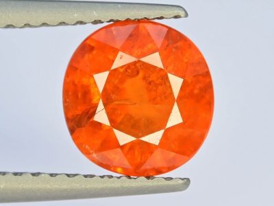 une image montrant un gros plan d'un diamant orange, avec une paire de pinces devant