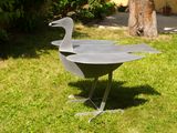 a metal sculpture of a duck on a stand in the grass