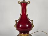 un vase rouge posé sur un socle doré, sur fond blanc