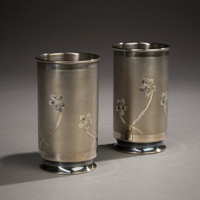 two silver cups with flowers on them sitting on a table