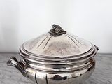 une cocotte ancienne en métal argenté avec son couvercle, posée sur une table en marbre