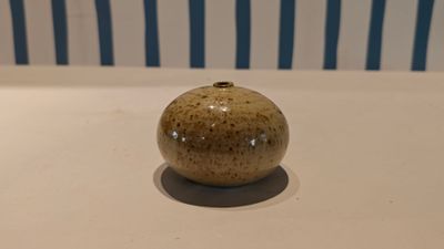 a small vase sitting on a table with a striped chair in the background