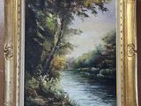 an oil painting of a river in a golden frame hanging on a wall