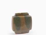 un petit vase marron et vert posé sur une surface blanche