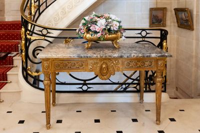 a marble table with a vase of flowers on it in front of a spiral staircase