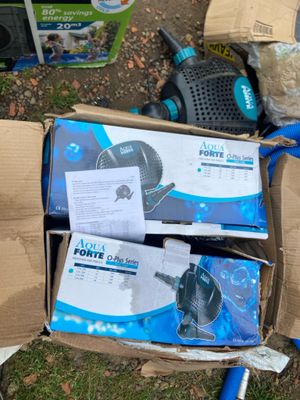 deux cartons contenant des pompes à eau et un tuyau posés par terre
