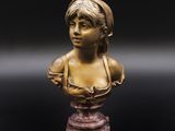 un buste en bronze représentant une jeune fille, posé sur un socle