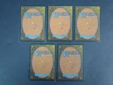 four magic the gathering cards are sitting on a blue surface