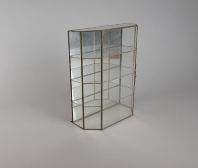 une vitrine en verre avec des bordures dorées et des étagères, posée sur un socle blanc