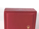 Le portefeuille rouge, orné d'une couronne, est posé sur une surface blanche.