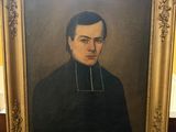 portrait d'un homme en manteau noir, dans un cadre doré, posé sur un plancher en bois