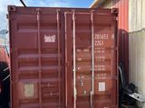un conteneur d'expédition rouge posé au milieu d'un champ, à côté d'un bâtiment