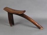 a small wooden stool with a curved seat on a gray surface