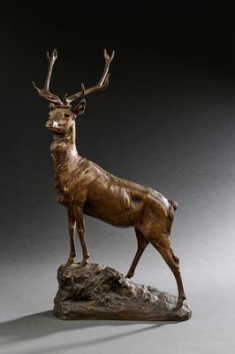 sculpture en bronze représentant un cerf debout sur un rocher, sur fond gris