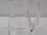 a clear glass pitcher with a handle on a table