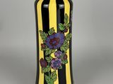 yellow and black striped vase with purple flowers and green leaves
