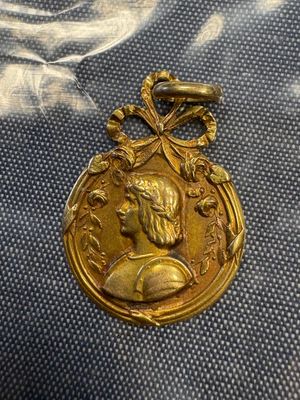 une vieille médaille en or sur laquelle est représenté le visage d'un homme, posée sur un tissu bleu