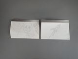 two pieces of paper with drawings on them sitting on a table