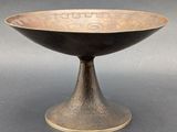 an antique bronze bowl on a pedestal on a gray background