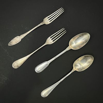 quatre cuillères en argent et une fourchette posées sur un fond noir