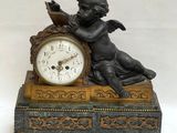 une statue représentant un Cupidon assis sur une table, à côté d'une horloge
