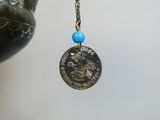 a silver coin with a blue bead hanging from a chain
