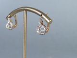 pair of gold and diamond earrings on a stand against a gray background