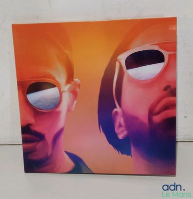 Deux hommes portant des lunettes de soleil se tiennent côte à côte devant un mur blanc.
