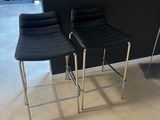 two black leather bar stools in a room with a black wall