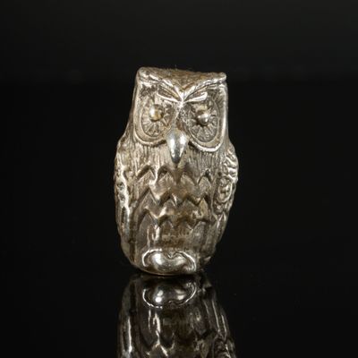 une figurine de chouette en argent posée sur une surface noire