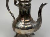 an antique silver tea pot with a bird handle on a white background