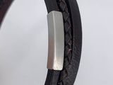 a close up of a leather bracelet with a metal bar on it