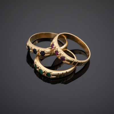 three gold rings with different colored stones on a black surface