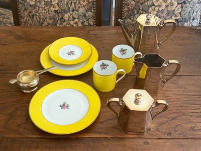 a wooden table with a yellow plate and cups and saucers on it