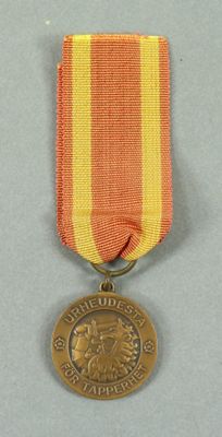 an old medal with a red, yellow, and white ribbon