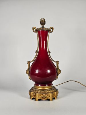 un vase rouge posé sur un socle doré, sur fond blanc