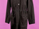un manteau noir posé sur un mannequin, devant un fond rose