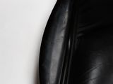 a close up of a black leather chair with a white wall in the background