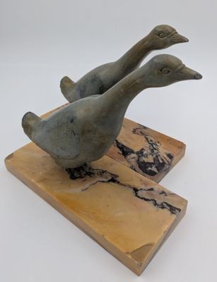 sculpture représentant deux canards perchés sur un bloc de bois posé sur une surface blanche