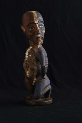 une vieille statue en bois représentant un homme assis sur un fond noir