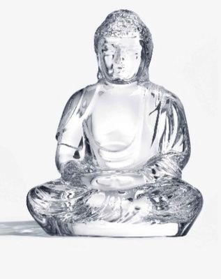 une statue en verre représentant un Bouddha assis sur une surface blanche