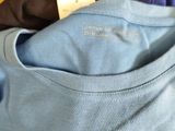 a blue shirt with a tag on it sitting on a pile of other shirts
